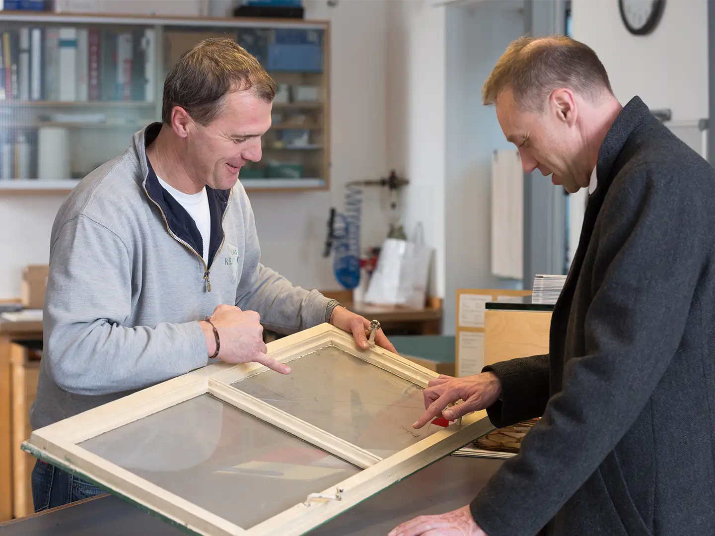 Glasermeister Günther Reisch im Gespräch mit einem Kunden einen Fensterflügel haltend