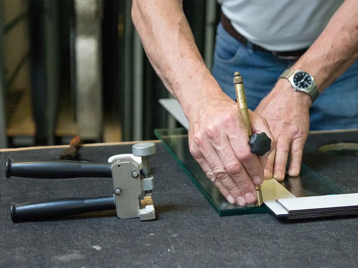 Günther Reisch schneidet Glas, zu sehen: Glaserwinkel, Schneideöl, Brechzange, Maßband