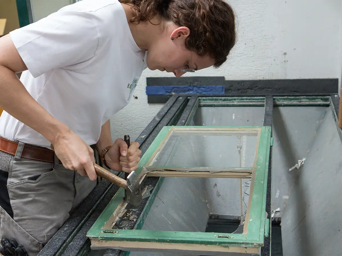 Mitarbeiterin bei Reparatur von Kastenfenster mit Aushaumesser und Hammer